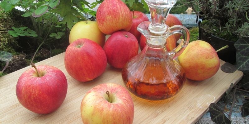 A rustic glass bottle of homemade apple cider vinegar with fresh apples showing pureloveandharmony and natural remedies