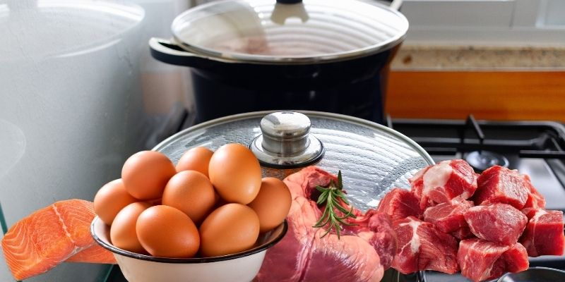 Preparation of a homemade slow-cook dog food recipe with whole eggs, raw beef heart, and ground beef on a stovetop with pots