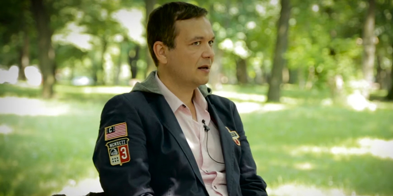 Sasha Riess sitting in a green park with a microphone during an interview representing clarity and spiritual freedom in work