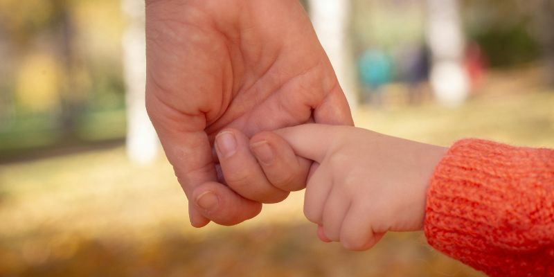 Close-up of father's hand holding child's small hand showing father doesn't have to be unhappy presence