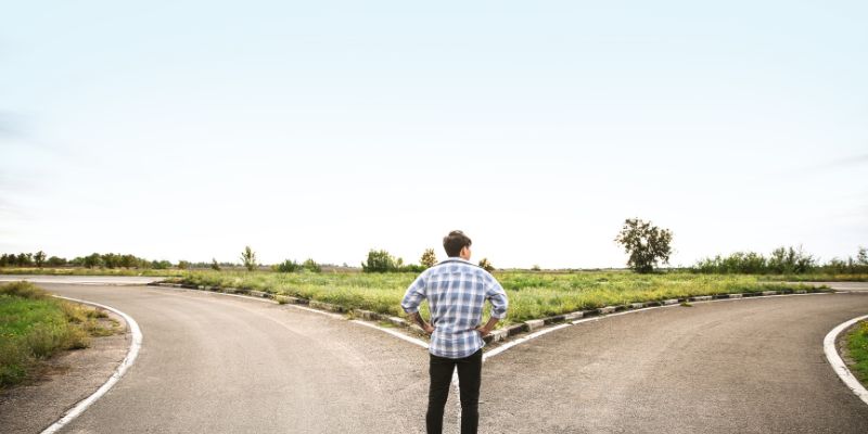 Man standing at a road fork representing choice and search for a better life inner direction