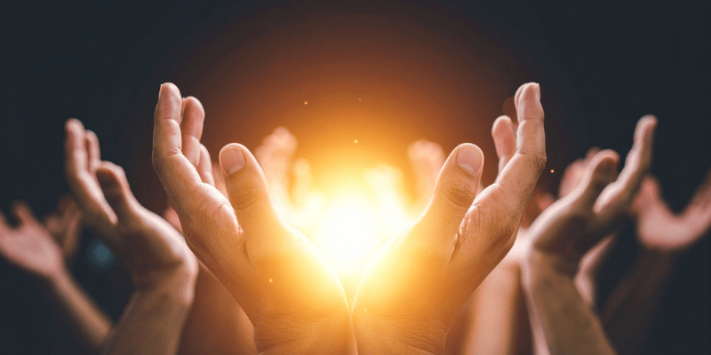 Multiple hands reaching towards a glowing warm light representing transgenerational trauma healing