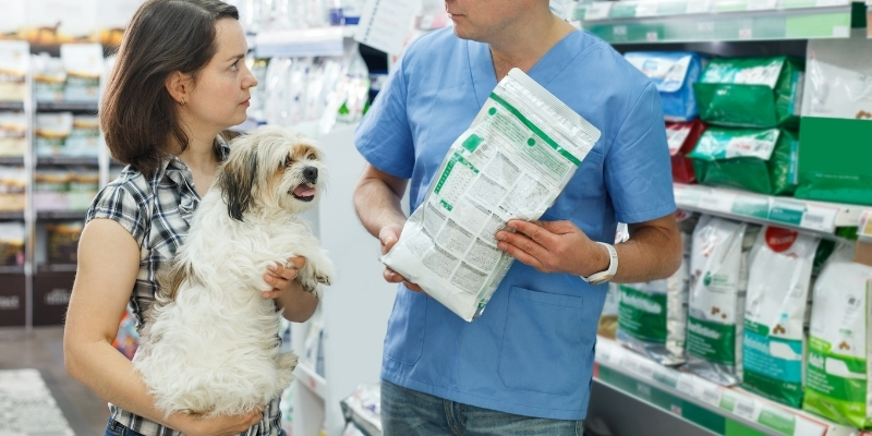 Dog owner holding small dog while examining a dog food bag label to understand war over dog food marketing